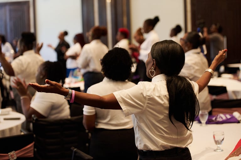 Group of people in white shirts with arms raised at an indoor gathering or celebration event