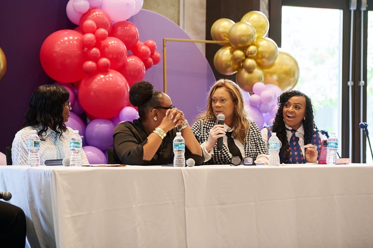 Panel of four women at a conference table with colorful balloons in the background