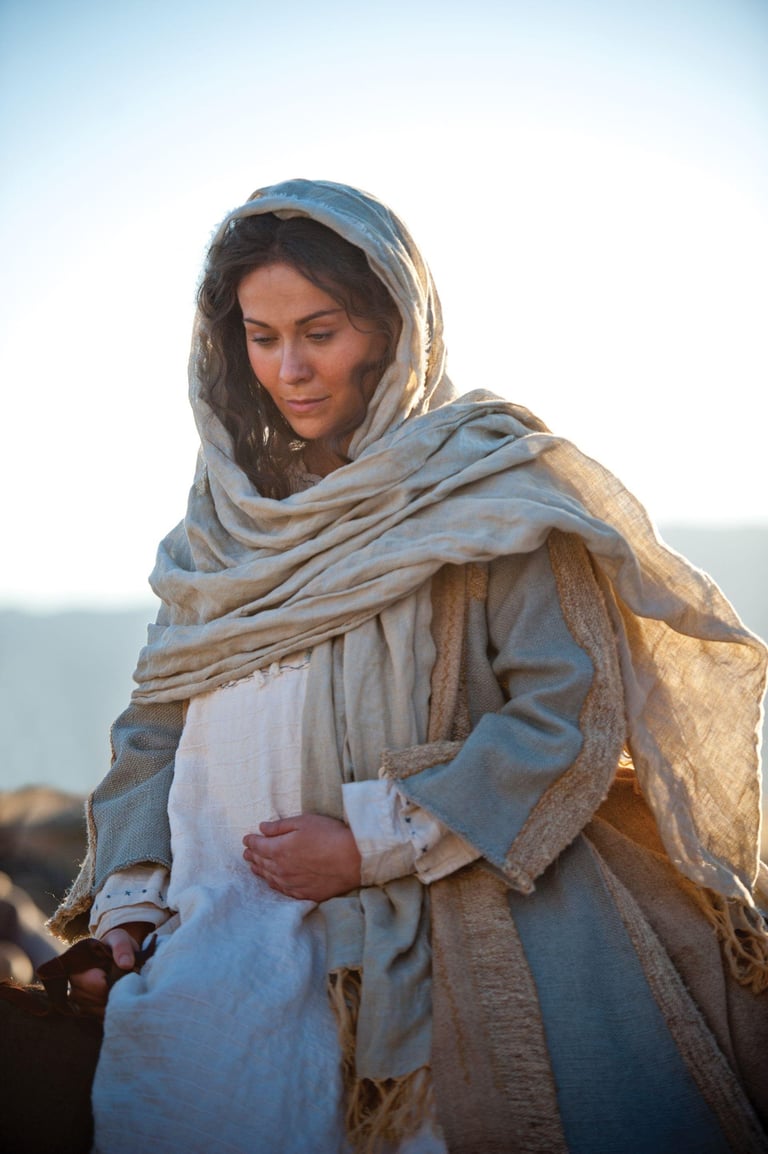 Woman wearing blue and beige draped clothing and headscarf, looking downward in golden sunlight against a clear sky